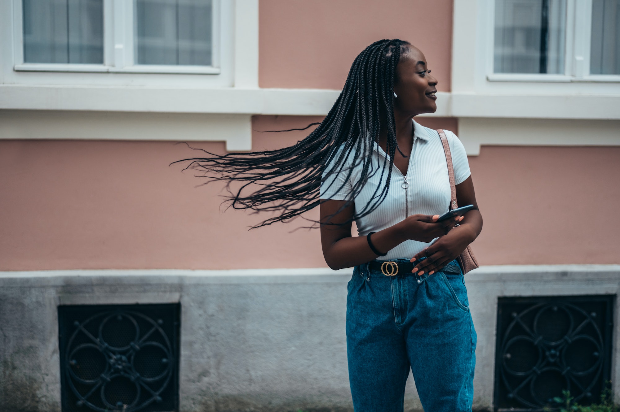 Beautiful african american woman using a smartphone and hair flipping her braids